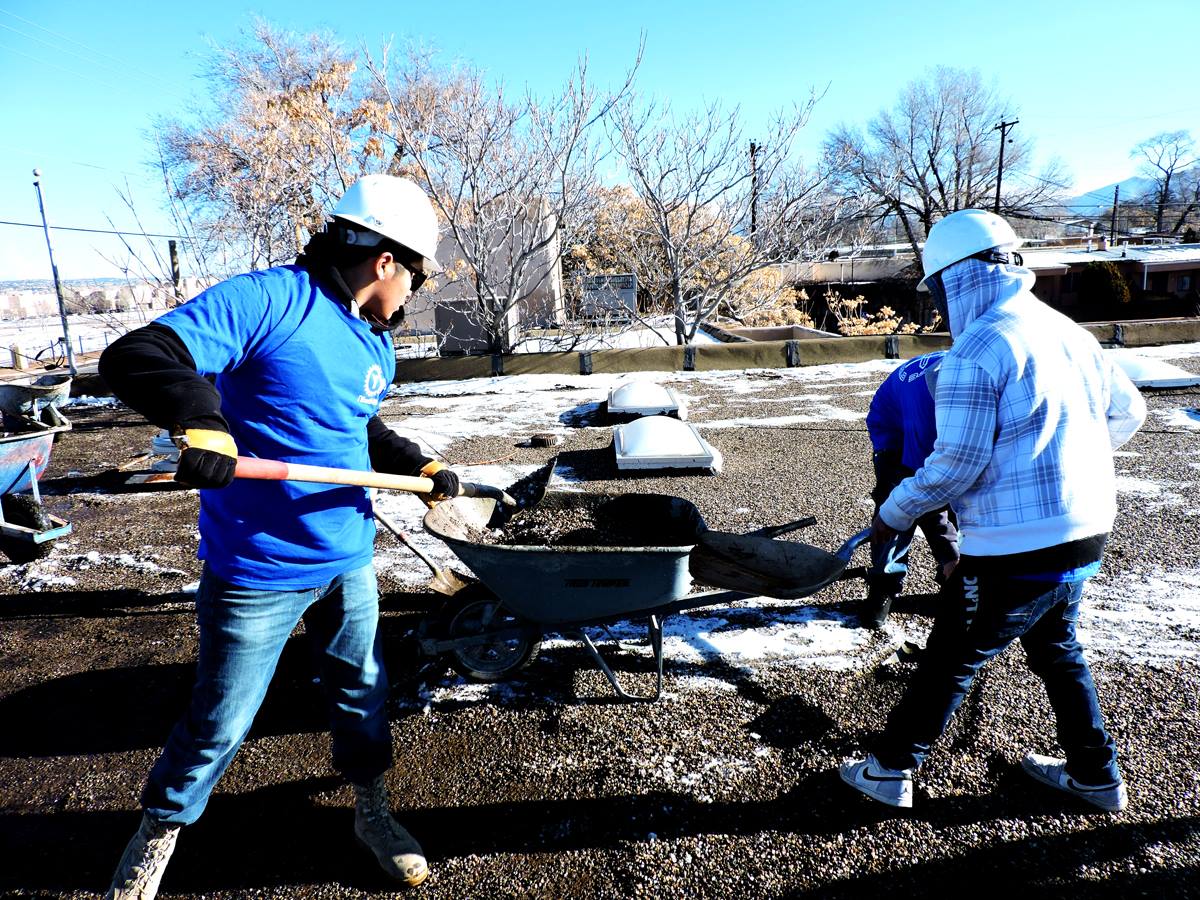 The YouthBuild crew carts away debris in preparation for installing the new roof.