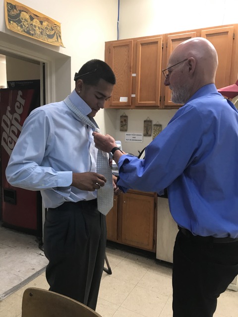 Juan gets a lesson in how to tie a tie.